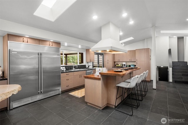 kitchen featuring vaulted ceiling with skylight, a center island, butcher block counters, island exhaust hood, and stainless steel appliances