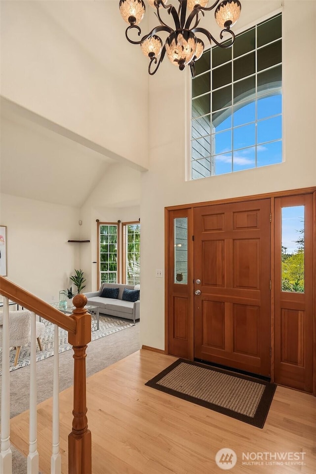 foyer entrance with high vaulted ceiling, an inviting chandelier, and wood finished floors
