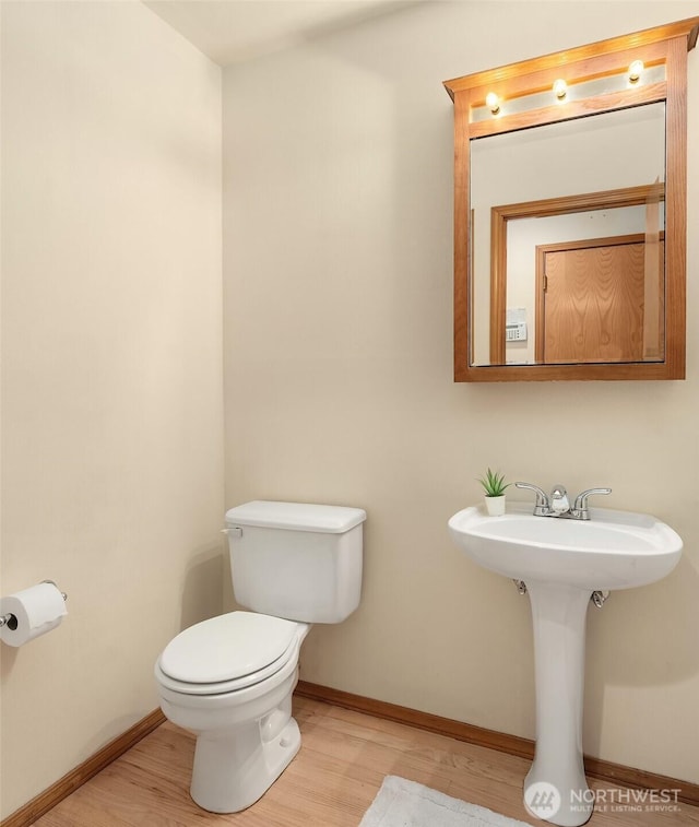 half bath with baseboards, toilet, and wood finished floors