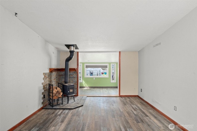 unfurnished living room with visible vents, a wood stove, wood finished floors, and baseboards