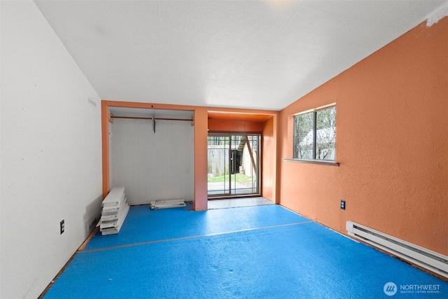 empty room with a textured wall, a baseboard heating unit, and lofted ceiling