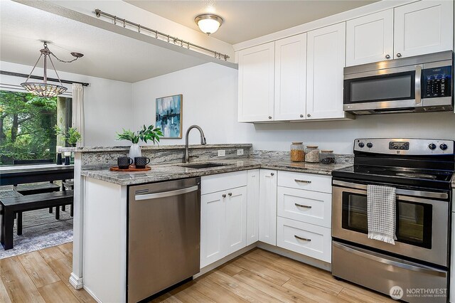 kitchen featuring stainless steel appliances, a sink, a peninsula, and light wood-style flooring