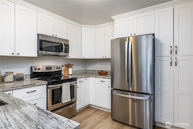 kitchen with appliances with stainless steel finishes, white cabinets, light wood-type flooring, and light stone counters