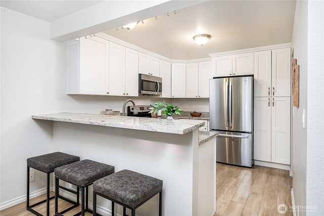 kitchen featuring appliances with stainless steel finishes, a peninsula, light wood-style floors, a kitchen breakfast bar, and white cabinets