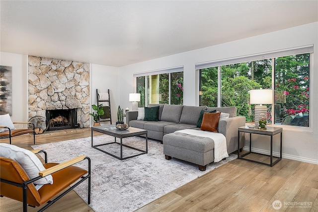 living area featuring light wood-style floors, a stone fireplace, and baseboards