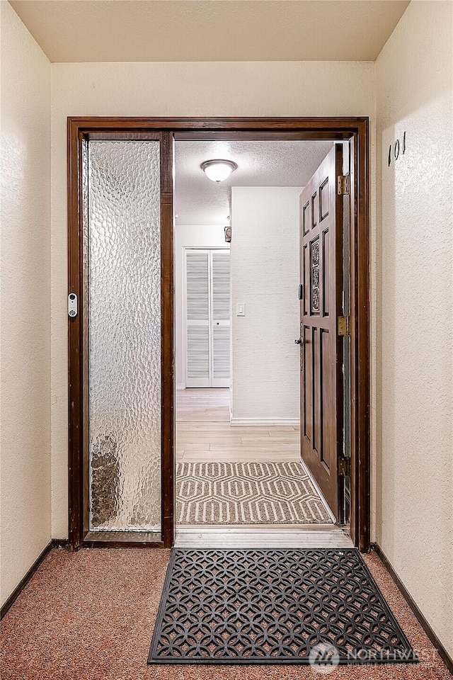 hall featuring baseboards and a textured wall