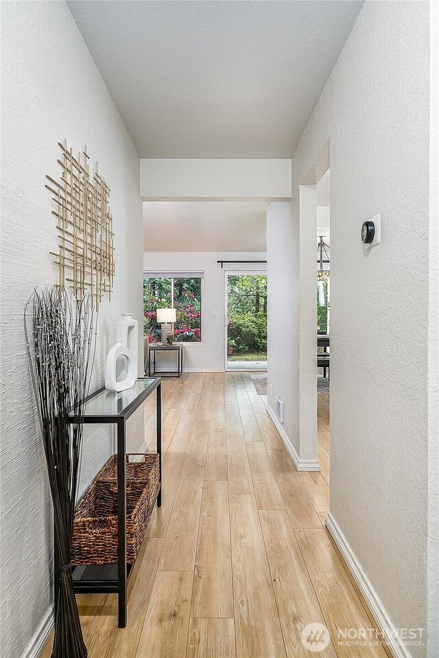 hall featuring light wood-style floors, a textured wall, and baseboards