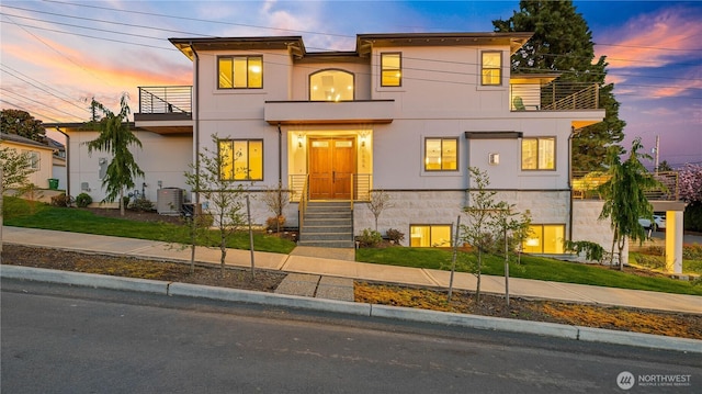 contemporary home with central AC, a front yard, a balcony, and stucco siding