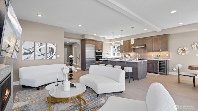 living area featuring recessed lighting, light wood finished floors, wine cooler, baseboards, and a lit fireplace