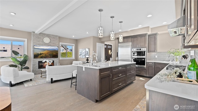 kitchen featuring light countertops, dark brown cabinets, a sink, beam ceiling, and appliances with stainless steel finishes