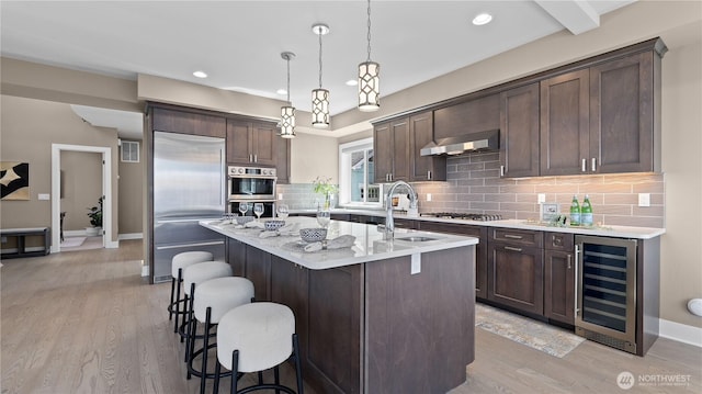 kitchen with dark brown cabinets, wall chimney range hood, beverage cooler, and stainless steel appliances