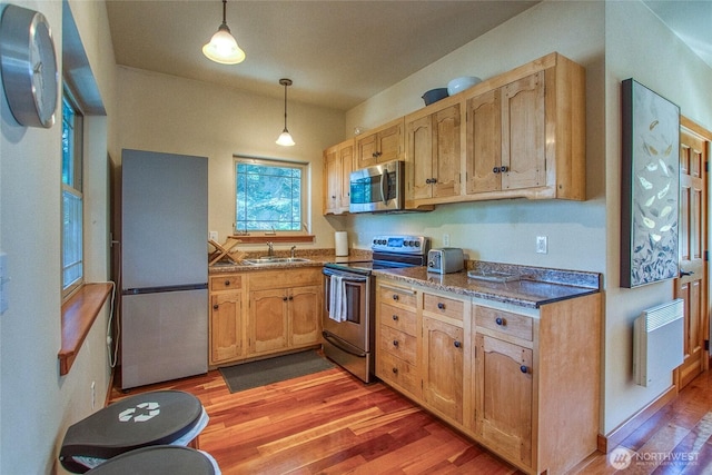 kitchen featuring dark stone countertops, decorative light fixtures, a sink, light wood-type flooring, and appliances with stainless steel finishes