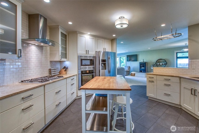 kitchen featuring glass insert cabinets, white cabinetry, wooden counters, wall chimney exhaust hood, and appliances with stainless steel finishes