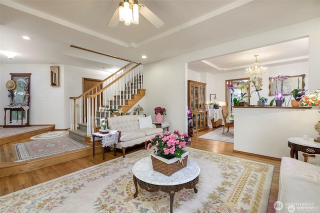 living room with recessed lighting, stairs, a tray ceiling, ceiling fan with notable chandelier, and wood finished floors