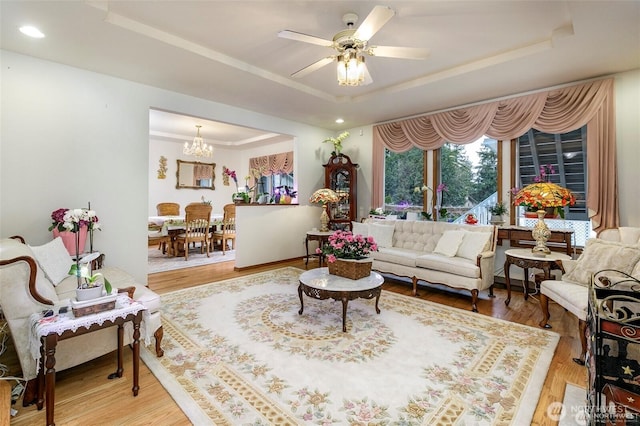 living room with a tray ceiling, recessed lighting, wood finished floors, and ceiling fan with notable chandelier