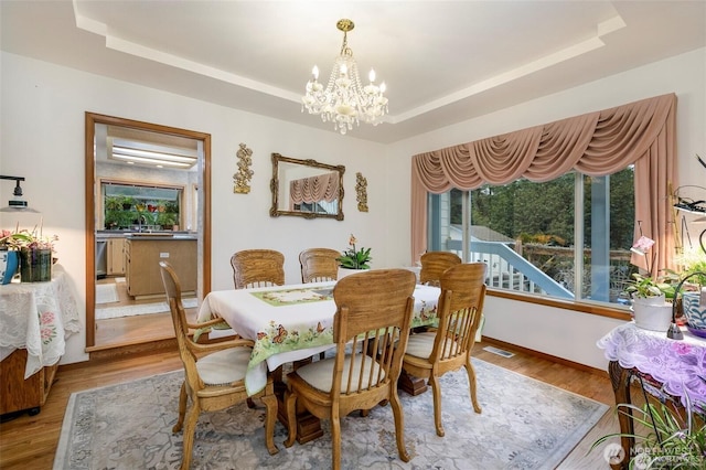 dining area with a tray ceiling, visible vents, a chandelier, wood finished floors, and baseboards