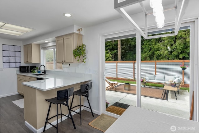 kitchen with dark wood-style flooring, black microwave, a sink, light countertops, and a kitchen bar