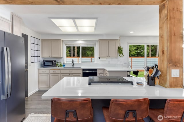 kitchen with a kitchen breakfast bar, wood finished floors, a sink, freestanding refrigerator, and black dishwasher