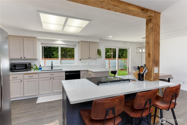 kitchen with a sink, light wood finished floors, black appliances, and a kitchen bar