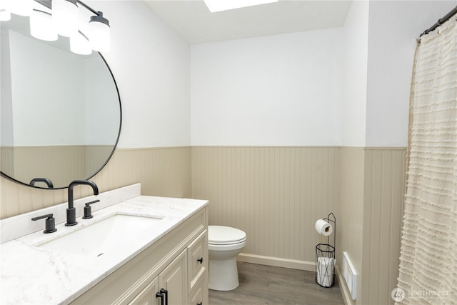 bathroom featuring toilet, wainscoting, wood finished floors, and vanity