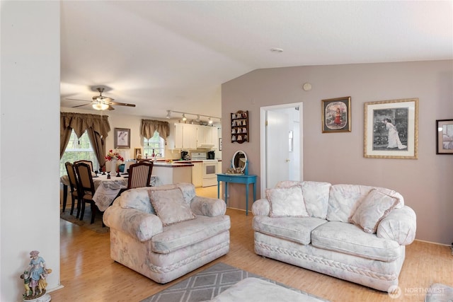 living room with light wood-style floors, rail lighting, ceiling fan, and vaulted ceiling