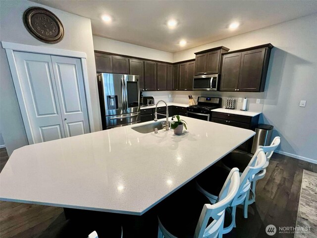 kitchen with a sink, light countertops, dark brown cabinetry, dark wood-style floors, and stainless steel appliances