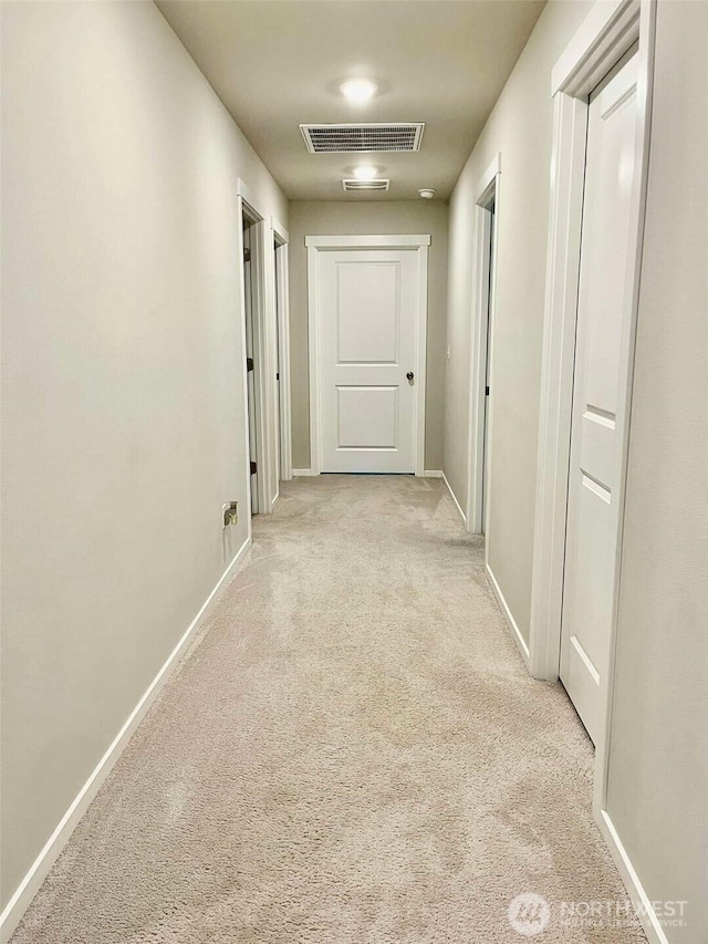 hallway with visible vents, baseboards, and light carpet