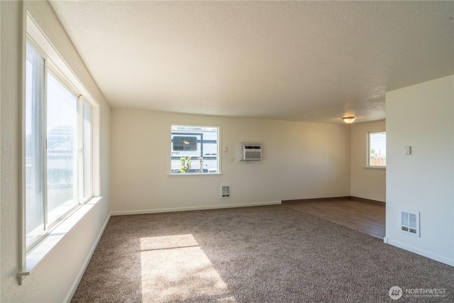 unfurnished room with a wall mounted air conditioner, a textured ceiling, carpet, visible vents, and baseboards