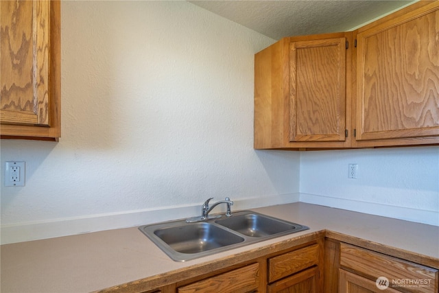 kitchen featuring brown cabinetry, a textured ceiling, light countertops, and a sink