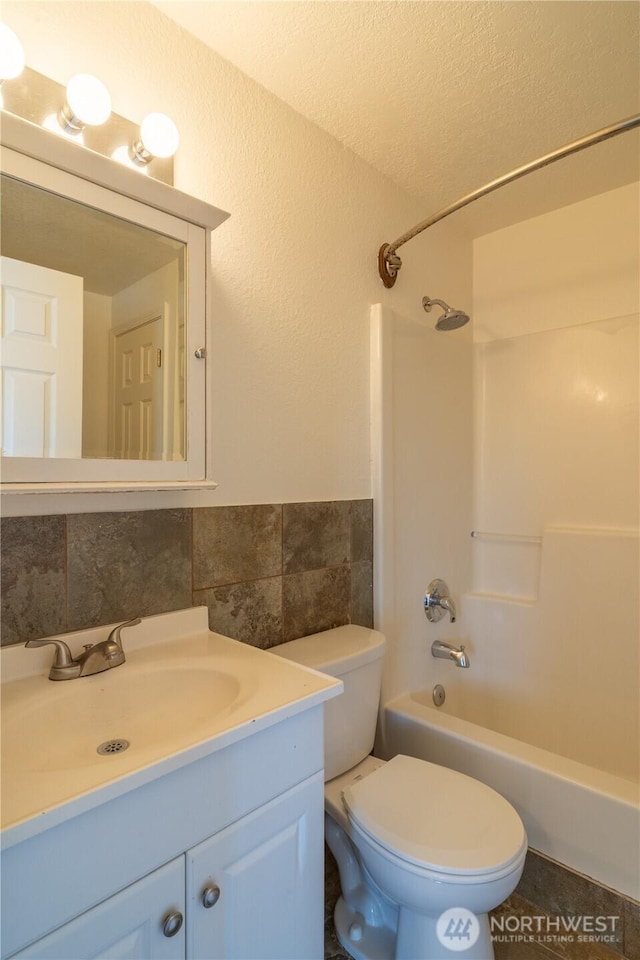 full bathroom with shower / bathing tub combination, tile walls, toilet, vanity, and wainscoting