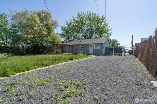 rear view of house featuring a gate, fence, and gravel driveway