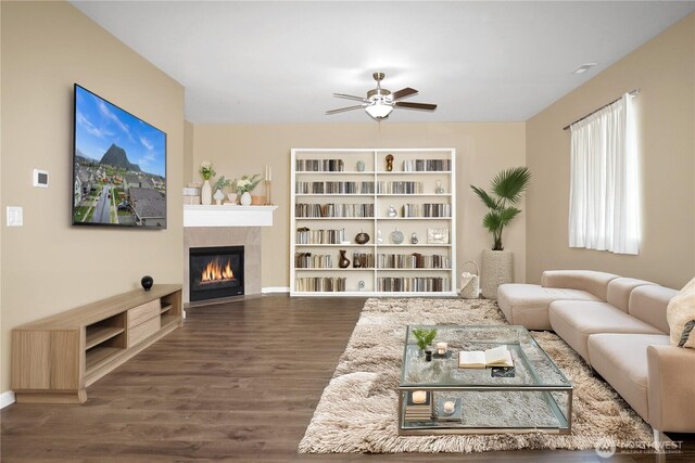 living area featuring baseboards, ceiling fan, a tiled fireplace, and wood finished floors