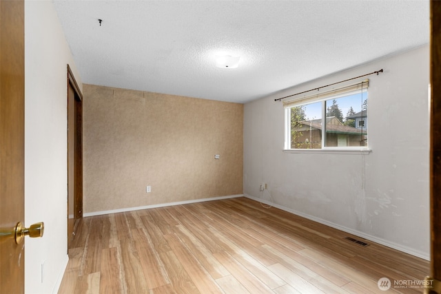 empty room featuring light wood-style floors, baseboards, visible vents, and a textured ceiling