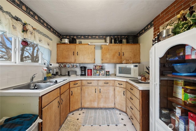 kitchen with white microwave, light countertops, a sink, and backsplash