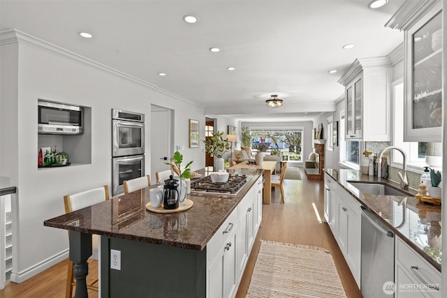 kitchen with light wood-style flooring, a sink, dark stone countertops, a kitchen island, and appliances with stainless steel finishes