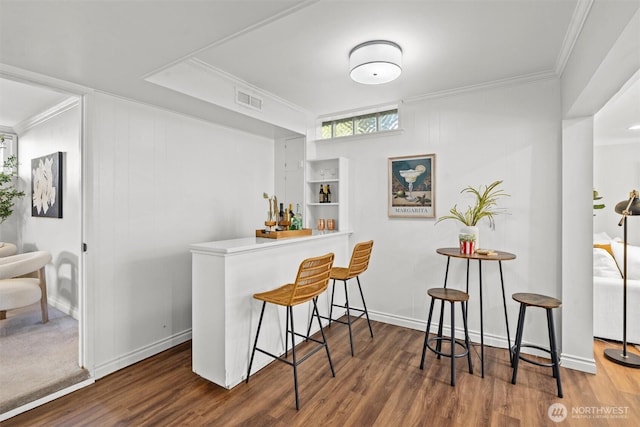 bar with crown molding, a dry bar, wood finished floors, and visible vents