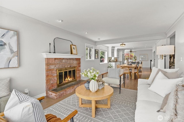 living area featuring crown molding, wood finished floors, ceiling fan, a fireplace, and baseboards