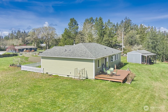 back of property with fence, a lawn, a shingled roof, a deck, and crawl space