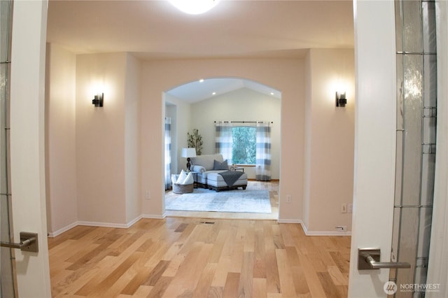 corridor with light wood-style flooring, arched walkways, baseboards, and lofted ceiling