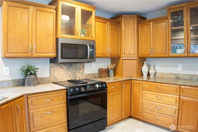 kitchen with stainless steel microwave, glass insert cabinets, black electric range, light stone countertops, and brown cabinets