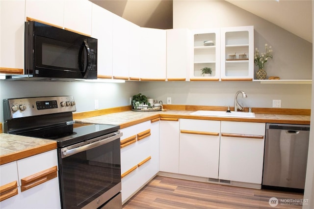 kitchen with appliances with stainless steel finishes, white cabinets, lofted ceiling, light wood finished floors, and a sink