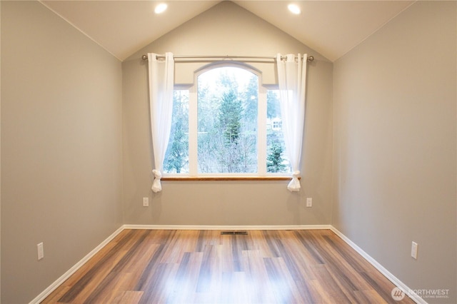 spare room with wood finished floors, visible vents, baseboards, and vaulted ceiling
