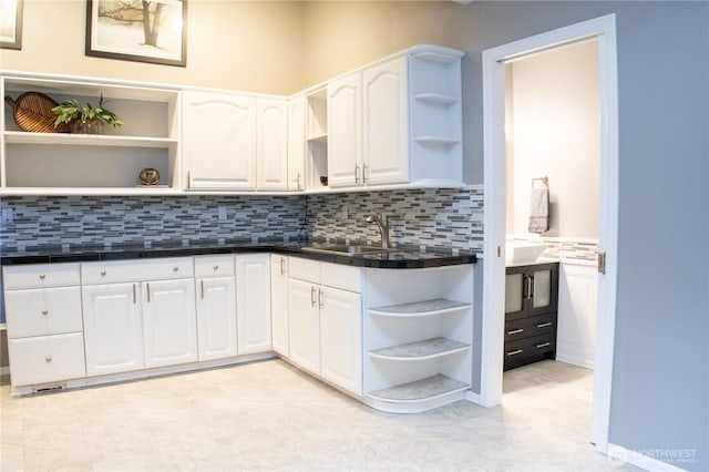 kitchen with backsplash, open shelves, dark countertops, white cabinets, and a sink