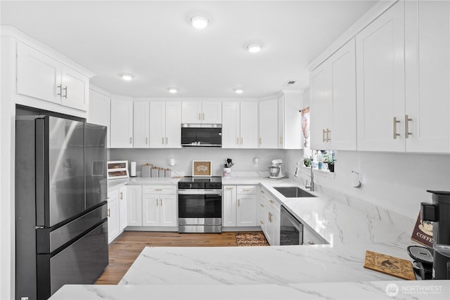 kitchen with light stone countertops, light wood-type flooring, white cabinetry, a sink, and appliances with stainless steel finishes