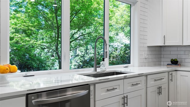kitchen featuring decorative backsplash, white cabinets, light stone counters, a sink, and dishwasher