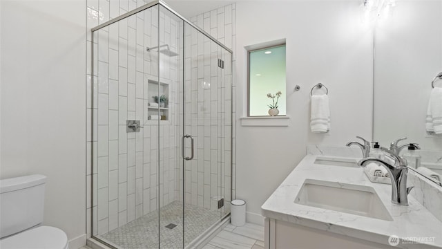 bathroom featuring double vanity, toilet, a shower stall, and a sink