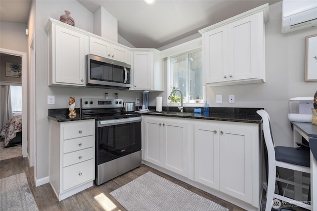 kitchen with a wall mounted AC, vaulted ceiling, white cabinetry, appliances with stainless steel finishes, and a sink