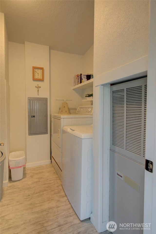 clothes washing area with laundry area, a textured ceiling, electric panel, light wood finished floors, and washing machine and dryer