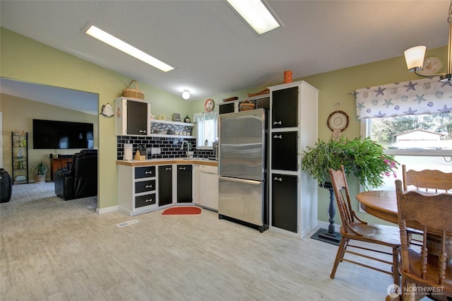 kitchen featuring open shelves, white dishwasher, freestanding refrigerator, backsplash, and lofted ceiling