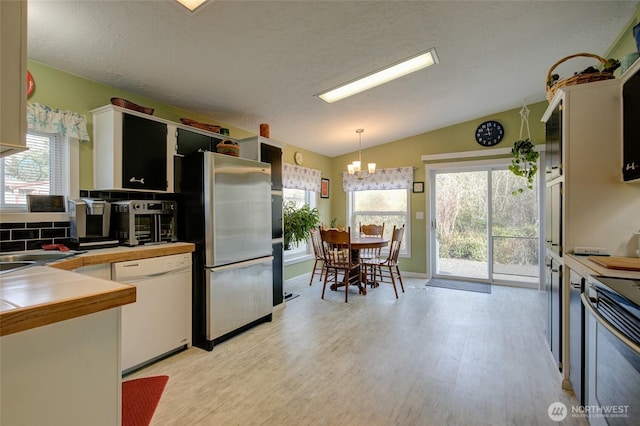 kitchen with lofted ceiling, a notable chandelier, light wood-style flooring, decorative backsplash, and stainless steel appliances